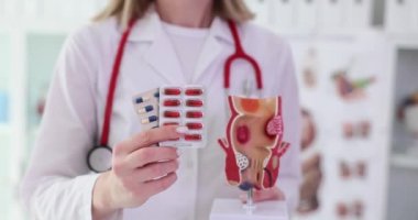 Deneyimli doktor elinde haplar ve rektum modeli tutuyor. Tıbbi üniforma uzmanı rektal hastalıklar için yavaş çekimde ilaç yazıyor.