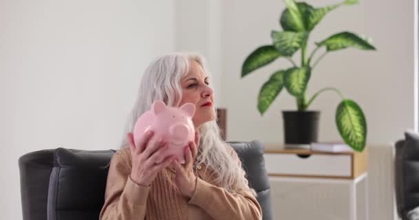 Smiling Mature Woman Shakes Piggy Bank Coins Living Room Positive — Stock Video