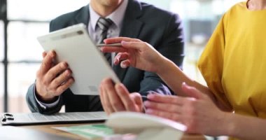 Kadın, meslektaşlarına görevlerini açıklıyor. Ofisteki tablet üzerinde veri gösteriyorlar. Müdür, iş yerindeki genç çalışanlara talimat veriyor.