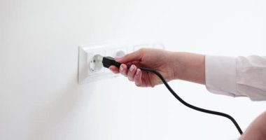 Kadın ofis odasındaki beyaz duvara yanlış priz takmaya çalışıyor. Bayan cihazları elektrik şebekesine bağlamıyor. Teknik detaylar