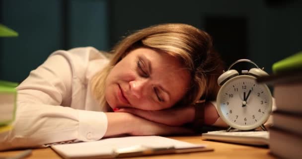 疲れている女性は ヴィンテージ目覚まし時計とノートとクリップボードの近くのテーブルで眠りに落ちる 眠い従業員はオフィスで夜遅くに滞在目を閉じます — ストック動画