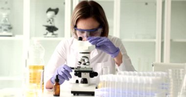 Laboratuvar çalışanı önemli bir araştırma için ayçiçeği yağı örneğini mikroskopla inceliyor. Kadın kadehte ağır çekimde sıvı hazırlıyor.