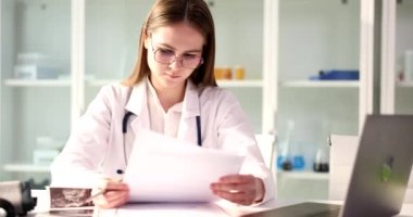 Profesyonel doktor klinikteki hastanın test sonuçlarını inceliyor. Kadın sonuçları ağır çekimde dizüstü bilgisayarla kontrol ediyor.