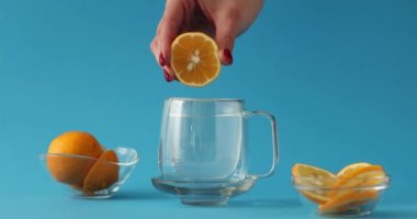 Mavi arka plan 4K filminde limon suyunu bir bardak suya sıkıştırmak ağır çekim. Soğuk algınlığının önlenmesi ve doğal C vitamini kavramı