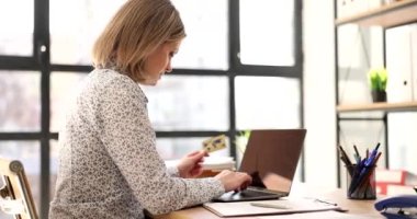 Sarışın kadın, iş yerindeki ağır çekimde kredi kartı ve laptop kullanarak internetten mal sipariş ediyor. Ofisteki internet servisinin parasını bayan ödüyor.