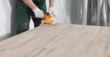 Yetenekli marangoz ahşap masa yüzeyini öğütücü makinesiyle parlatır. Profesyonel üniformalı bir erkek ahşap işlemek için ekipman kullanır.