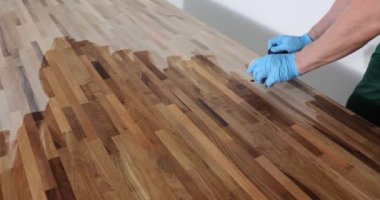 Erkek marangoz ahşap ofis masasının yüzeyini özel cila ile kaplar. İş üniformalı bir adam sıvıyı ağır çekimde bez parçasıyla süpürüyor.