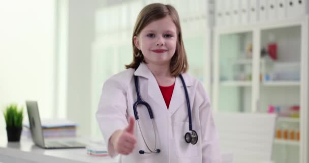 Χαμογελαστό Κοριτσάκι Λευκό Παλτό Μιμείται Ρόλο Του Γιατρού Και Δείχνει — Αρχείο Βίντεο