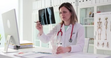 Tıp alanındaki kadın profesyonel hasta avuç içi kemiklerinin röntgen görüntülerine bakıyor. Üniformalı doktor yavaş çekimi dikkatlice inceliyor.