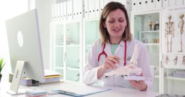 Steteskoplu kadın doktor el iskeletinden bahsediyor. Tıp alanında uzman hafif hastane ofisinde kol iskeleti sunuyor.