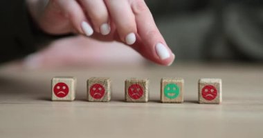 Kadın parmağı, bulanık arka planda negatif yüz ifadesi olan bloklara karşı yeşil pozitif emojili ahşap küpü hareket ettirir