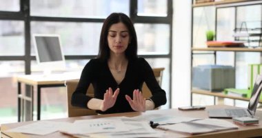 Kadın ofis çalışanı avuç içlerini katlar ve meditasyon yapmaya başlar. Yorgun esmer kadın sakinleşmeye çalışıyor ve aydınlık ofis odasında çalışmaya odaklanıyor.