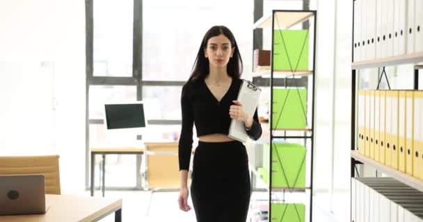 女性Olは 光を前提にカメラに向かってまっすぐに歩いていく 職場でデータノートを持っている若い従業員スローモーション — ストック動画