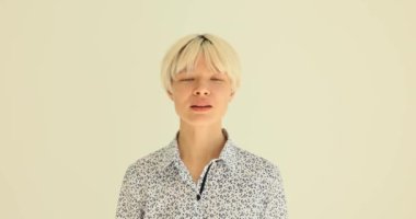 Klasik bluzlu genç bir kadın, onaylamak için başını sallıyor. Kısa sarı saçlı bayan, sarı duvarda ağır çekimde duran hareketleri onaylıyor.