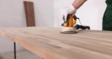 Lastik eldivenli işçi yeni ahşap masayı öğütme makinesiyle parlatıyor. Kapalı alanda ağır çekimde ligneous yüzeyleri cilalamak için profesyonel ekipman