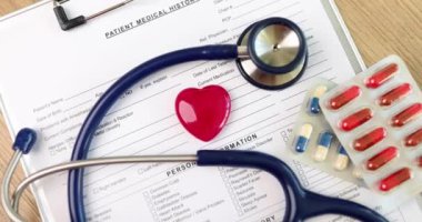 Kırmızı kalp oyuncak figürü steteskopun yanında yatıyor ve hasta tedavisi ile ilgili belgelerin üzerinde haplar var. Tıbbi ekipman ve kalp hastalıkları konsepti