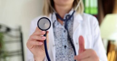 Memnun doktor steteskopu elinde tutuyor. Kadın, klinikte ağır çekimde duran tıbbi ekipmanların kullanılabilirliğini onaylıyor