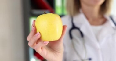 Beyaz önlüklü kadın doktor klinikte taze sarı elma tutuyor. Steteskoplu hoş sarışın kadın sağlıklı beslenme öneriyor.