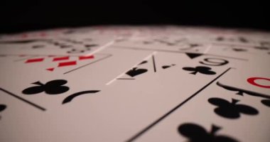 Poker destesi düzensiz bir şekilde hafif ışık altında yüzeye dağılmış. Yeni oyundan önce doğruluğu kontrol etmek için masaya konulan farklı takım elbiseli poker kartları