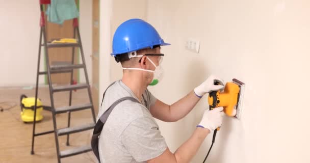 ヘルメットと保護マスクの専門家は 研削盤と壁を処理します アパートの遅い動きで壁を研磨するための専門機器 — ストック動画
