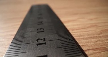 Tahta masadaki uzunluğu ölçmek için parmakları ve çizgileri olan metal cetvel. Odadaki masa başında tamirci var. Elle çalışan ustabaşı araçları