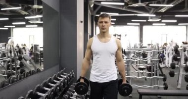 Spor salonu 4K filminde ağır çekimde dambılları elinde taşıyan bir erkek sporcu. Düzenli spor eğitimi konsepti
