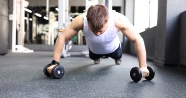 Spor salonu 4K filminde dambıllarla şınav çeken erkek sporcu. Vücut konsepti için düzenli sıralama yükü