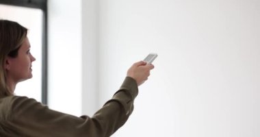 Kadın elinde uzaktan kumandayla klimayı işaret ediyor. İklim Kontrol Odası