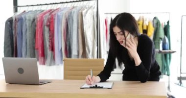 Çamaşırhane çalışanı telefonda konuşuyor ve emir yazıyor. Müdür kuru temizleme kıyafetlerini kontrol ediyor.