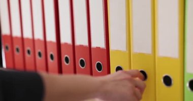 Kadın, dosyaları ve kağıtları olan klasörler halinde klasörleri seçiyor. Ofis raflarındaki bir sistem tarafından yönetiliyor