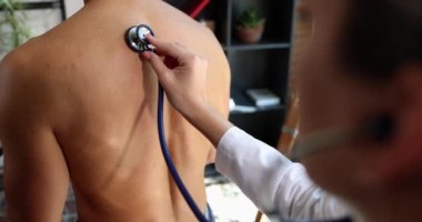 Terapist steteskopla nefes alan insanları dinler. Bronşit hastasının nefes alışını dinleyen bir terapist.