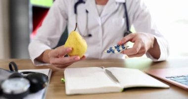 Doktor beslenme uzmanının elinde armut ve vitamin hapları var. Kozmetik uzmanı sağlıklı organik gıdaları vitaminlerle yemeyi tavsiye ediyor.