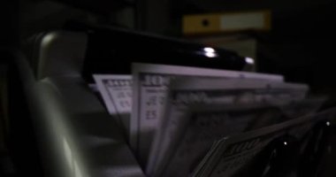 Karanlık arka planda nakit saymak için banka makinesine yakın çekim. 100 dolarlık banknotlar döviz ve makine para sayar.