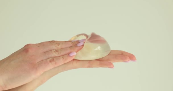 ベージュ地に柔らかいシリコン胸インプラントを絞る女性の手 女性患者は 診療所のスローモーションで乳房手術の準備 — ストック動画