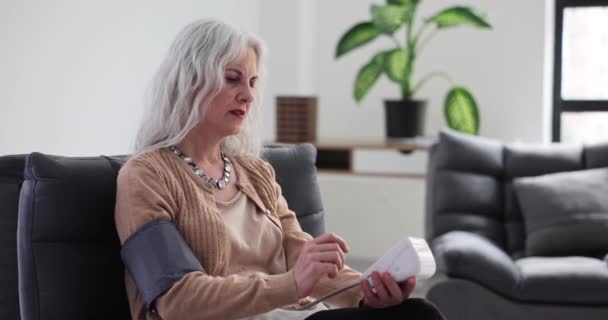 成熟的女人在家里坐在扶手椅上 用数字测压仪来测量血压 老年患者慢动作现代医疗设备 — 图库视频影像