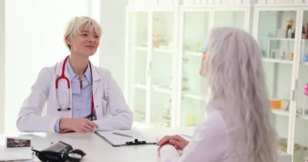Médica Sorridente Aperta Mão Uma Paciente Madura Sentada Mesa Mulheres — Vídeo de Stock