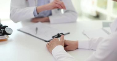 İş üniformalı kadın doktor klinikte destekleyen olgun bir müşterinin elini tutuyor. Kadın hasta sağlık durumundan endişe ediyor yavaş çekimde şikayet ediyor