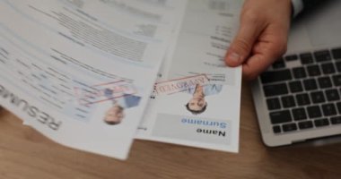 Yönetici, şirketteki yeni iş pozisyonu için başvuranların özgeçmişlerini inceler. Dizüstü bilgisayarın yanında özgeçmiş belgelerini ağır çekimde elinde tutan adamın elleri.