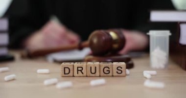 Kadın yargıcın not almasına karşı tahta küplerden yapılmış kelime ilaçları. Narkotik etkisi olan beyaz kapsüller ve masada tokmak. Uyuşturucu trafiğine ilişkin mahkeme duruşması