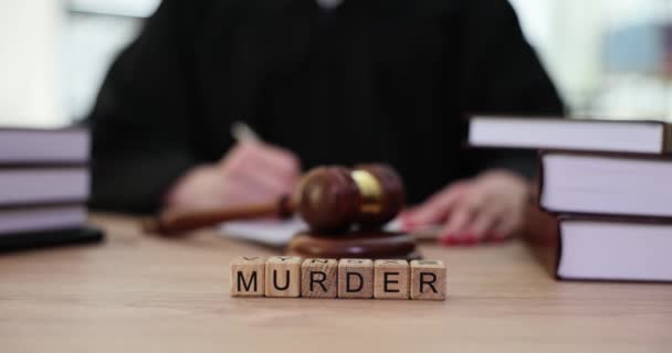 女性の裁判官が書類を記入することに対して木製のキューブで作られた言葉殺人 犯罪者の裁判と判決 命を奪う罰 — ストック動画