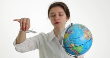 Dünya 'nın yanında oturan oyuncak uçakla oynayan kadın beyaz duvarın karşısında seyahat etmeyi hayal ediyor. Seyahat acentası kavramı ve yavaş çekim ülkelere uçuşlar