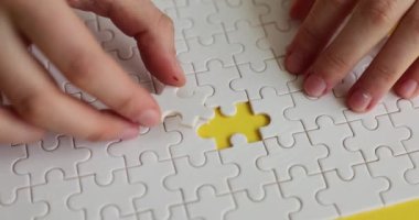 Kadın eli, kayıp parçayı sarı arka plandaki beyaz bulmacanın içine yerleştiriyor. Mükemmel bir iş stratejisi bulmak. Çözümlerin başarılı kombinasyonu yavaş çekim