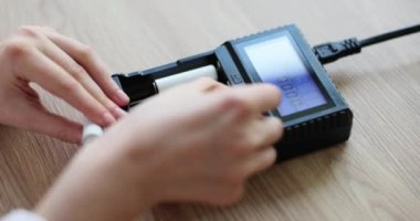 Kadın elleri şarj aletine batarya takmak için hücreleri yerleştiriyor. Ahşap masadaki batarya gücünü arttırmak için bir cihaz. Elektronik aygıtların yavaş çekimde çalışması için destek