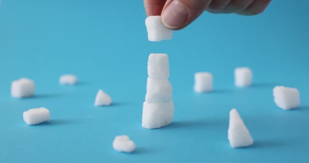 雄鱼的手在蓝色的背景上 用不同形状的白色精制糖块做成塔楼 人们调查甜食产品的特性 — 图库视频影像
