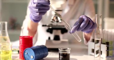 Lastik eldivenli kadın bilim adamı, pipetten ham yağ örneğini laboratuvar odasındaki masada oturan tüpe döküyor. İş yerinde ağır çekimde kadın deneyleri