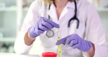 Lastik eldivenli kadın kimyager asit oranını ölçmek için test çubuğunu sıvıyla tüpe sokuyor. İş üniformalı kadın madde örneğini yavaş çekimde inceliyor.