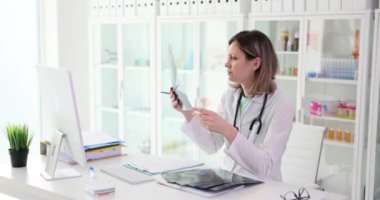 İş üniformalı doktor klinikteki masada oturan kemik kırığının röntgenini inceliyor. Kadın çalışan ağır çekimde radyografa bakıyor.