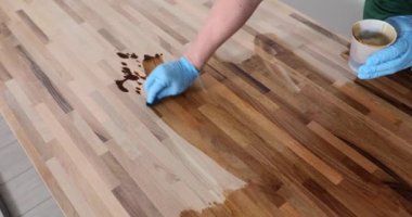 Eldivenli işçiler, vernikli ahşap zemin yüzeyi olan cilalayıp iş yerinde duruyorlar. Adam ahşap yavaş çekim işlemek için sıvı vernik kullanır.