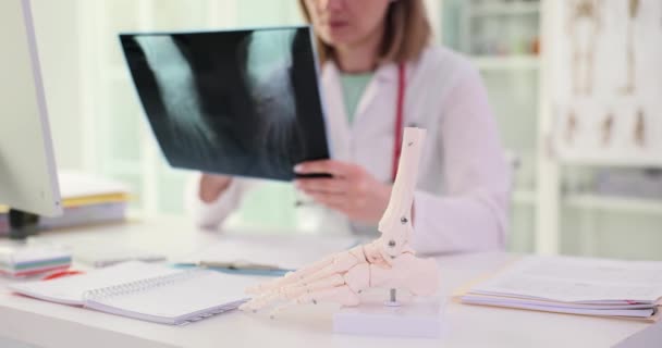Врач Осматривает Рентген Рядом Моделью Скелета Ноги Сидя Белым Столом — стоковое видео