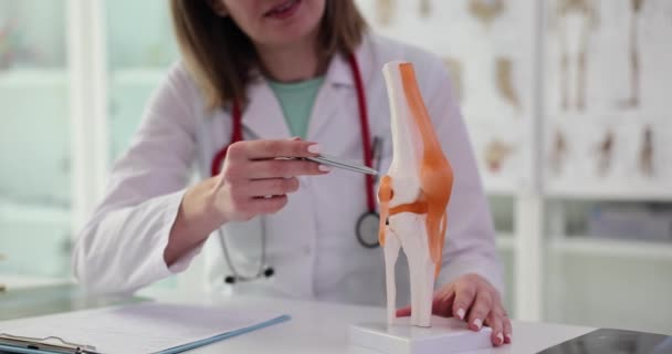 女性医師は 現代の診療所に座って骨格に膝の仕事を説明します 関節スローモーションの仕事について聴診器を持つ医学の専門家 — ストック動画